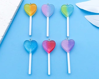 Può includere: Sei lecca-lecca a forma di cuore con dettagli glitterati. I lecca-lecca sono di vari colori, tra cui giallo, rosa, verde, blu e viola. I lecca-lecca sono su uno sfondo blu.