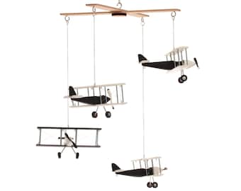May include: A hanging mobile featuring four biplane models suspended from a wooden cross frame. Each biplane is constructed with black and white components, including wings, a fuselage, a propeller, and landing gear, all connected by thin strings.