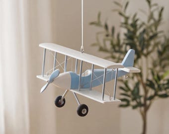 May include: A hanging biplane model featuring a white and light blue color scheme. The aircraft has two stacked wings, a front propeller, and two black wheels attached to the landing gear. Thin wires connect the wings, and a string suspends it.