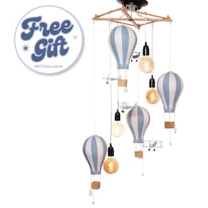 May include: A hanging light fitting featuring four fabric hot air balloons with light blue and white vertical stripes, wooden baskets, and small model aeroplanes suspended from a wooden frame with three glowing Edison-style light bulbs.