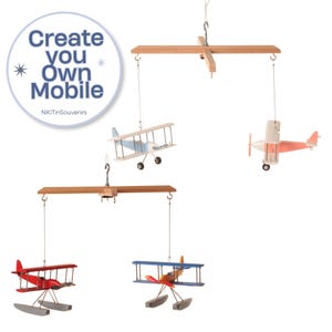 Puede incluir: Un móvil colgante con cuatro aviones de juguete de madera suspendidos de dos travesaños de madera. Los aviones están pintados en rojo, azul y blanco. Un gráfico circular en la esquina muestra el texto Create you Own Mobile NiKiTinSouvenirs.