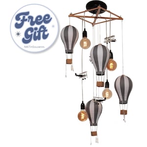 May include: A ceiling light fixture featuring four fabric hot air balloons with grey and white vertical stripes, wooden baskets, and small model aeroplanes suspended from a wooden frame, interspersed with three exposed filament light bulbs.