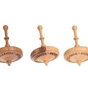 Op de afbeelding: Drie houten tollen met een centrale steel en een ronde basis. Elke tol is voorzien van de tekst "GLEBOOS" en "HAND CRAFTED IN UKRAINE" gegraveerd langs de rand van de houten schijf. De tollen variëren in houtnerfkleur van licht tot donkerbruin.