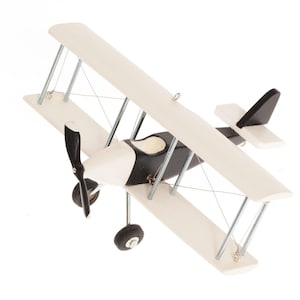 Pode incluir: Um modelo de avião biplano com um esquema de cores preto e branco. A aeronave possui duas asas sobrepostas, uma hélice preta e duas rodas de aterragem. Hastes metálicas finas ligam as asas e um pequeno ilhó metálico está fixado na asa superior.
