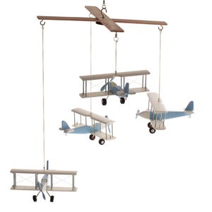 May include: A hanging mobile featuring four biplane models suspended from a wooden crossbar. Each biplane is painted in light blue and white with small black wheels and propellers. The planes are attached to the frame by thin white strings.