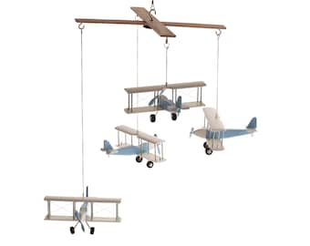 May include: A hanging mobile featuring four biplane models suspended from a wooden crossbar. Each biplane is painted in light blue and white with small black wheels and propellers. The planes are attached to the frame by thin white strings.