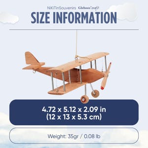 May include: A wooden biplane model with a propeller, two wings, and wheels, suspended by a string. Text reads SIZE INFORMATION, NiKiTinSouvenirs Gleboos craft, 4.72 x 5.12 x 2.09 in, and Weight: 0.08 lb. The plane features a light brown wood finish.