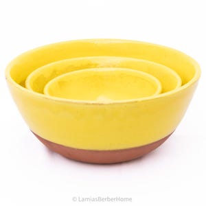 May include: A set of three nesting bowls. The bowls are yellow with a reddish-brown base. The bowls are of different sizes, with the smallest bowl nested inside the middle bowl, which is nested inside the largest bowl.