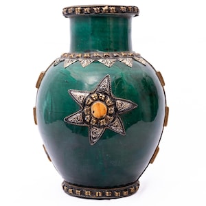 May include: A green ceramic vase with silver and gold-toned metal detailing. The vase has a star-shaped embellishment and decorative bands. The vase has a glossy finish and a rounded shape. The vase is approximately 25 cm tall.