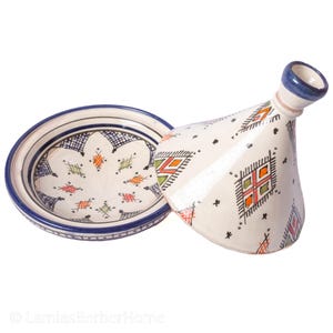 May include: A white ceramic tagine with a blue and white geometric pattern. The tagine has a lid with a small spout. The tagine is a traditional Moroccan cooking pot.