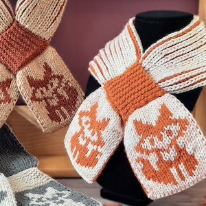 May include: Two knitted scarves with a fox pattern in shades of brown, orange, and white. The scarves are tied in a bow shape.