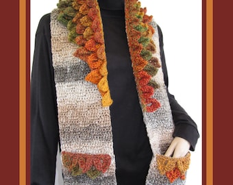 May include: A crocheted scarf with a leaf design in shades of green, orange, and brown. The scarf has pockets on the ends and a wide collar.