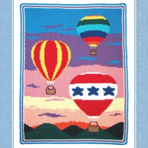 May include: A colorful crochet wall hanging featuring three hot air balloons against a sunset sky. The balloons are red, yellow, and blue with white stripes and stars. The sky is a gradient of purple, pink, and yellow.