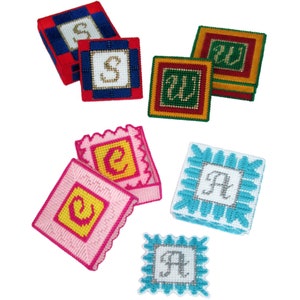 Puede incluir: Seis pequeñas cajas cuadradas con diferentes telas de colores y letras bordadas. Las cajas están decoradas con diferentes patrones y colores. Las letras son "S", "W", "C", "A", "S", y "A".