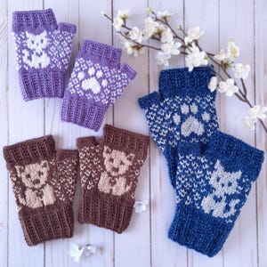 Puede incluir: Guantes sin dedos de punto en tonos morado, marrón y azul, cada uno con un diseño de animal único. Los guantes muestran un patrón de gato, huella de pata y oso de peluche en blanco o beige. Los guantes están colocados sobre una superficie de madera clara.
