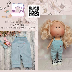 May include: PDF sewing pattern for overalls for a 30 cm doll. The pattern is for Mia 'Nines d'Onil' dolls. The image shows a doll wearing a pair of light blue overalls with a red pocket.
