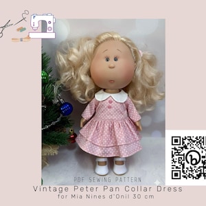 May include: A doll wearing a pink polka dot dress with a white Peter Pan collar and white shoes. The doll has blonde curly hair and is standing in front of a Christmas tree. Text on the image reads "Vintage Peter Pan Collar Dress for Mia Nines d'Onil 30 cm."
