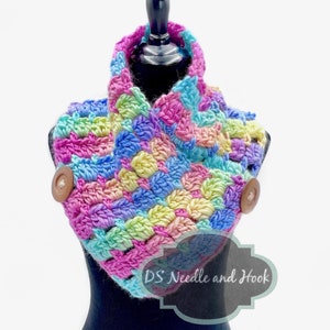 May include: A colorful crocheted cowl with a rainbow pattern and two wooden buttons. The cowl is displayed on a black mannequin. The text "DS Needle and Hook" is visible on a black label.