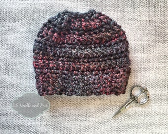 Peut inclure: Un bonnet en crochet de couleur gris foncé, noir et rouge. Le bonnet est fait avec un fil épais et a un design simple et ample.
