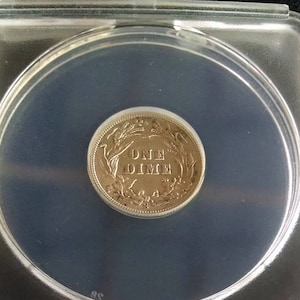 May include: A silver US dime coin with the inscription "ONE DIME" surrounded by a wreath of leaves and a wheat stalk.