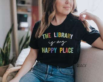 May include: A black short-sleeved t-shirt featuring the multi-colored text THE LIBRARY is my HAPPY PLACE printed on the front. The word THE LIBRARY is in a sans-serif font, is in a cursive script, and HAPPY PLACE is in a bold sans-serif font.