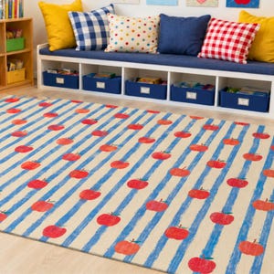 May include: A rectangular area rug featuring a repeating pattern of red apples arranged in rows over a background of vertical, textured blue stripes on a light beige surface. The design covers the entire visible area of the floor covering.
