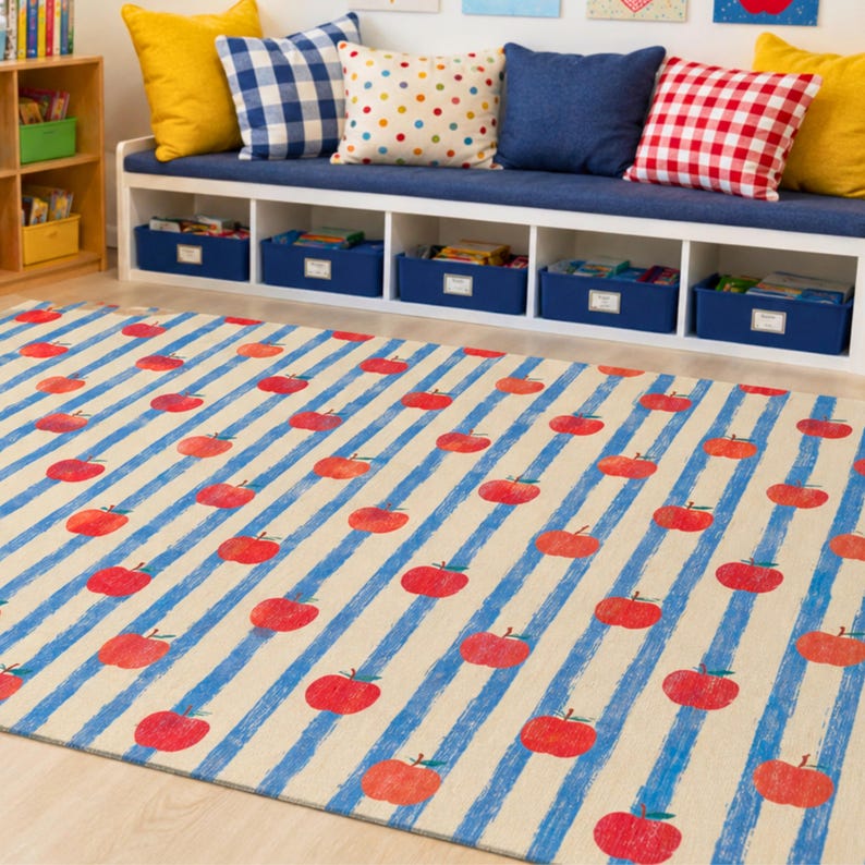 May include: A rectangular area rug featuring a repeating pattern of red apples arranged in rows over a background of vertical, textured blue stripes on a light beige surface. The design covers the entire visible area of the floor covering.