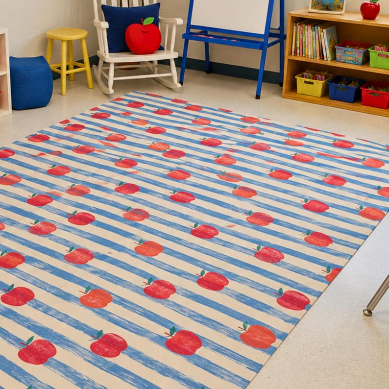 May include: A rectangular area rug featuring a repeating pattern of red apples with green stems arranged over a background of horizontal light blue and off-white stripes. The rug covers a portion of the floor in a room with light-colored flooring.