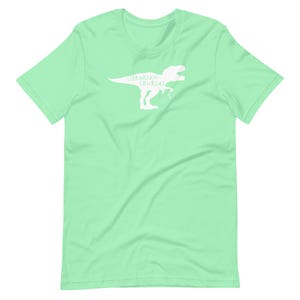May include: A light green t-shirt featuring a white silhouette of a Tyrannosaurus Rex with the words "Librarian Saurus" printed on it. The shirt is made of a soft material and has a crew neck.