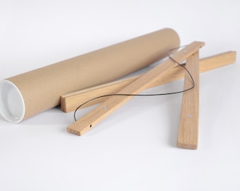 May include: A brown cardboard poster tube with a white interior, alongside wooden poster hangers. The hangers are made of light-colored wood and connected by a black string. The items are on a white surface.