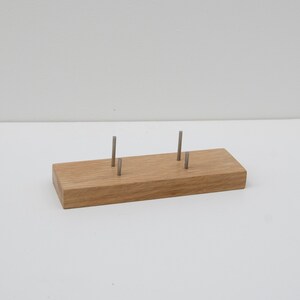 Puede incluir: Un expositor rectangular de madera con cuatro postes met&aacute;licos. El expositor es de madera de color marr&oacute;n claro y est&aacute; dise&ntilde;ado para sujetar objetos peque&ntilde;os. Los postes met&aacute;licos est&aacute;n espaciados uniformemente y parecen ser de metal plateado.