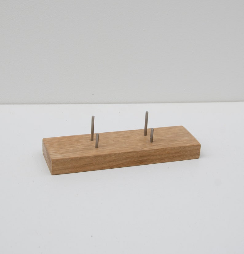Puede incluir: Un expositor rectangular de madera con cuatro postes met&aacute;licos. El expositor es de madera de color marr&oacute;n claro y est&aacute; dise&ntilde;ado para sujetar objetos peque&ntilde;os. Los postes met&aacute;licos est&aacute;n espaciados uniformemente y parecen ser de metal plateado.