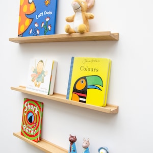 May include: Wooden floating shelves displaying children's books and small wooden figurines. The books include "Hooray for Fish!", "Ten Little Fingers and Ten Little Toes", "Shark in the Park!", and "Colours". A stuffed animal mouse sits on the top shelf.