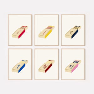 May include: Six framed art prints featuring matchbox illustrations. Each matchbox is open, displaying matches and text in various colors. The text includes words like "sutgers" and "free". The matchboxes are set against a cream-colored background.