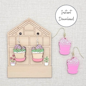 Könnte beinhalten: Holzohrringe in Form von rosa Blumentöpfen mit grünen und lila Blumen. Die Ohrringe werden auf einem ohrringhalter in Form eines Gewächshauses aus Holz präsentiert. Die Worte "Instant Download" stehen in einem weißen Kreis.