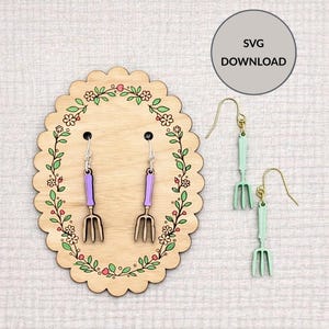 May include: Wooden earrings in the shape of garden forks, with purple handles and silver hooks, displayed on a wooden oval with floral accents. Additional earrings in mint green are also shown. The image includes the text "SVG DOWNLOAD".