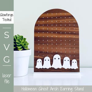 May include: A wooden arch earring stand with a ghost theme. The stand has a brown wood finish and is decorated with white ghost silhouettes. The stand has a white base and is designed to hold earrings.