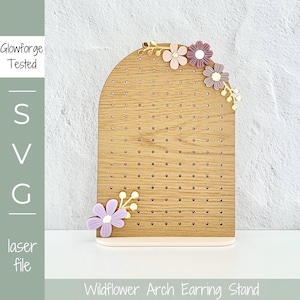 May include: Wooden arch earring stand with a light wood finish and a white base. The stand is decorated with purple and pink flowers and gold leaves. The text "Wildflower Arch Earring Stand" is printed below the stand.