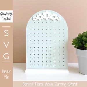 Puede incluir: Un expositor de pendientes de color azul claro con un diseño de arco floral blanco. El expositor tiene una base blanca y está hecho de madera. Tiene una cuadrícula de agujeros para sujetar los pendientes.