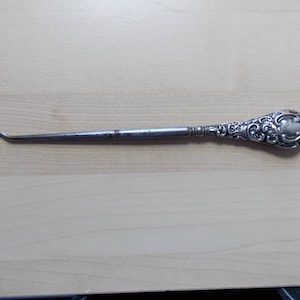 Peut inclure: Un chausse-pied en argent avec une poignée ornée et gravée. La poignée a une forme ovale arrondie.