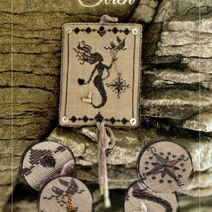 May include: A cross-stitch design featuring a mermaid holding a compass and a bird, with the word "Siren" above. The design is framed with a decorative border and includes the text "Designed and stitched by Viktoriia Popovych."