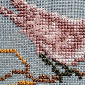 May include: Close-up of a cross-stitch embroidery featuring a pink flower with green leaves and a yellow flower with brown stems.