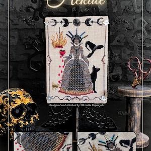 May include: Cross-stitch design featuring the word "Hekate" in elegant script. The artwork depicts a figure in a gown, a black cat, and other symbolic elements. The design is displayed on a stand with a black skull and decorative scissors.