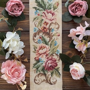 May include: A vintage-style floral tapestry with a beige background and colorful flowers, framed in a gold metal frame with a ring at the bottom.
