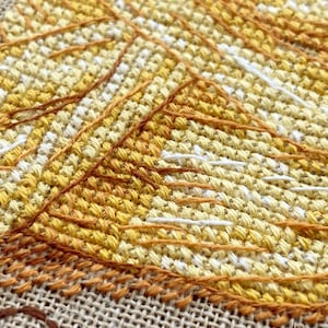 Puede incluir: Primer plano de un dise&ntilde;o de bordado de punto de cruz con una serie de puntadas superpuestas de color amarillo, naranja y blanco, creando un efecto texturizado y en capas.
