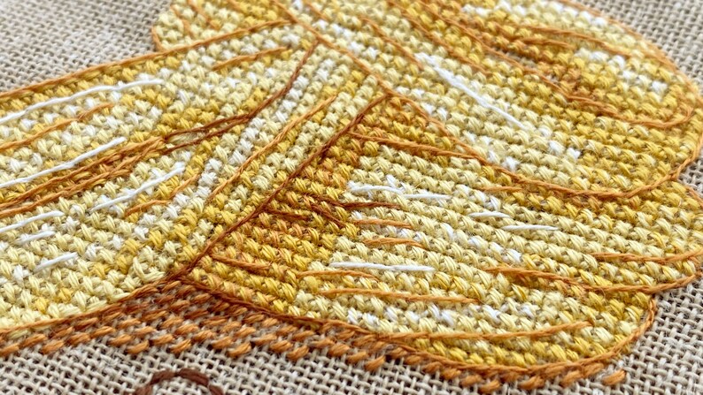 Puede incluir: Primer plano de un dise&ntilde;o de bordado de punto de cruz con una serie de puntadas superpuestas de color amarillo, naranja y blanco, creando un efecto texturizado y en capas.