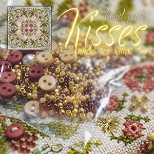 May include: A bead pack with the text "Kisses under the willow tree" features a variety of craft supplies. The image includes beige buttons, gold and brown beads, and a small cross-stitch design with red and green floral patterns.