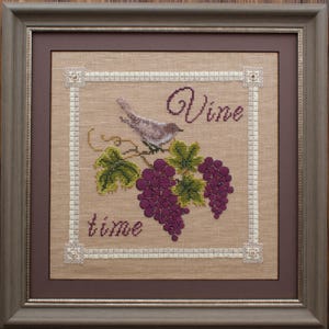 May include: Framed cross-stitch art featuring a bird perched on a grapevine with purple grapes and green leaves. The words "Vine time" are stitched in a decorative font. The artwork is framed in a brown wooden frame.