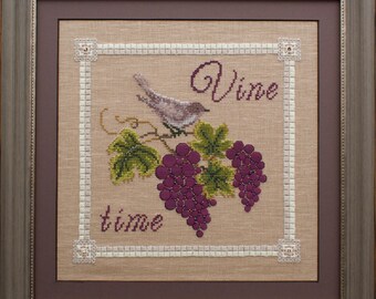 May include: Cross-stitch artwork in a wooden frame, depicting a bird on a grapevine with purple grapes and green leaves. The words "Vine time" are stitched in a decorative font. The frame is brown.