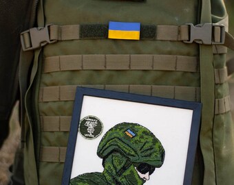 Pode incluir: Uma mochila militar verde com um remendo da bandeira ucraniana e um bordado emoldurado de um soldado usando um capacete e uniforme de camuflagem.